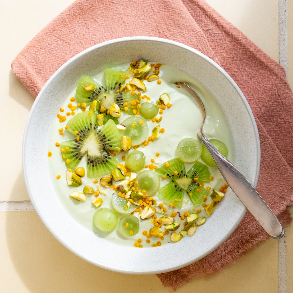 Top view of fruit yogurt bowl recipe in white bowl with kiwi and grapes and bee pollen
