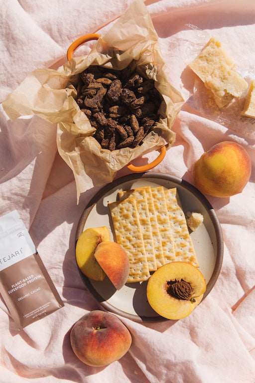 A plate of sliced peaches and crackers with a basket of dried cacao seeds beside.