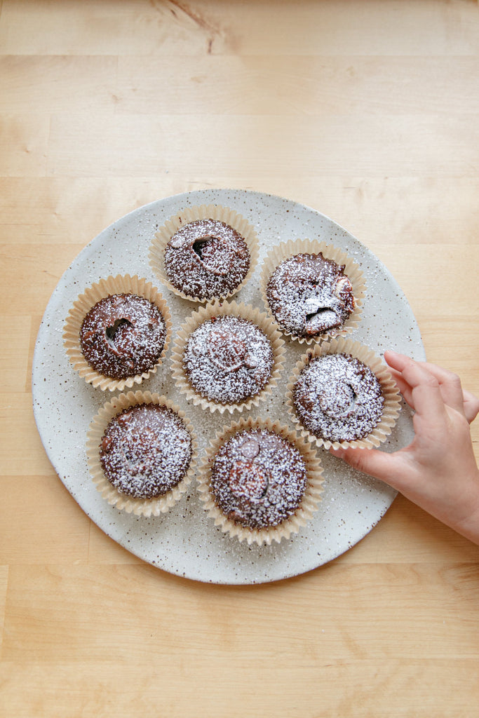 Chocolate Cupcakes Dusted with Powdered Sugar on a White Plate, and a Hand Reaching for a Cupcake