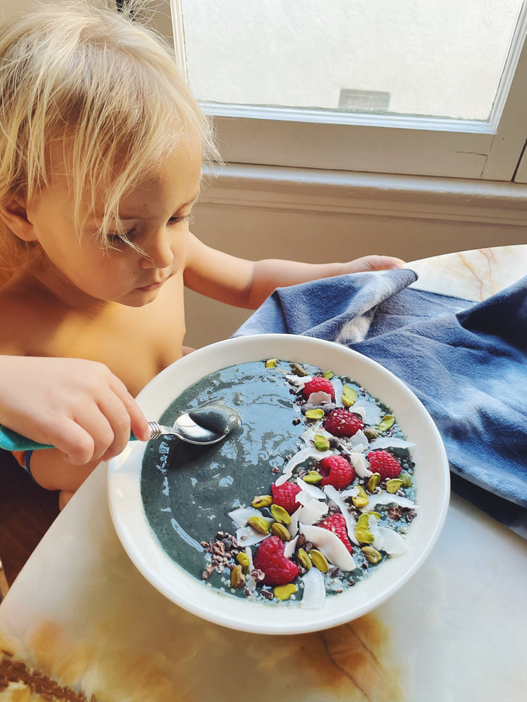 Young Child Sitting By the Window at the Breakfast Table  Eating a Smoothie Style Breakfast with Raspberries and Coconut Shaving From a Bowl s